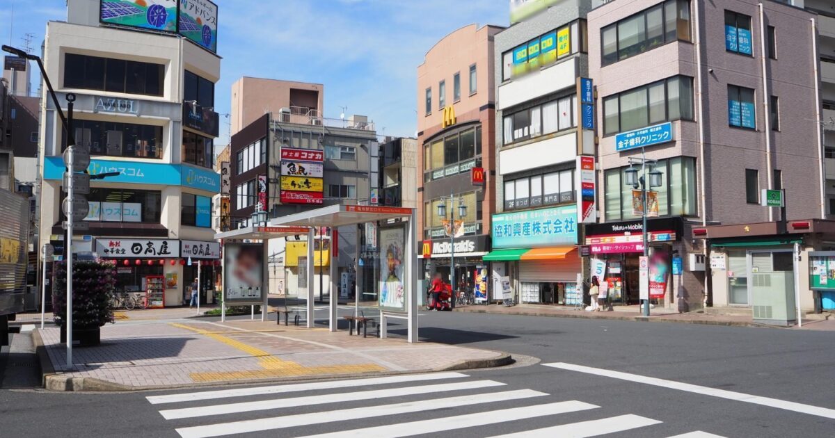 下町のバス停と飲食店が立ち並ぶ駅前風景